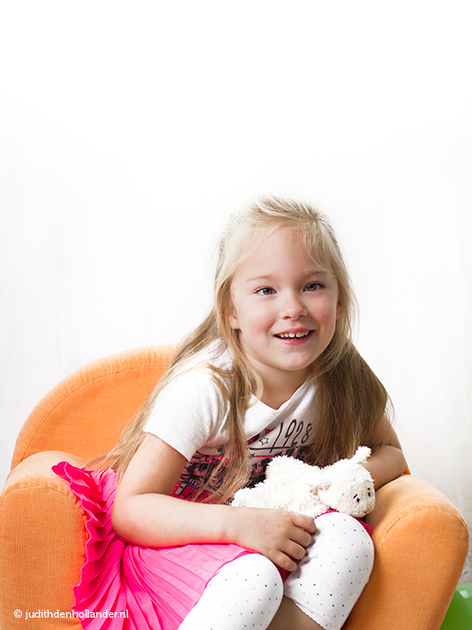In-Home photoshoot | Young girl with a toy in an orange chair against a light background | In-huis fotoshoot Hoofddorp | Fotografie J. den Hollander.