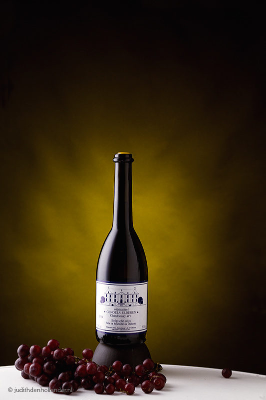 Professionele Wijnflessen Fotografie | Sfeerbeeld wijnfles met druiven | Productfoto met impact | Vakfotografie WijndomeinFotografen Limburg | Belgische Chardonnay.